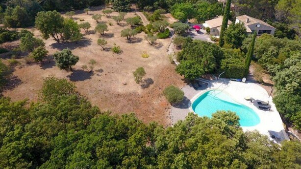Ett flygbildsfoto av en fastighet med en swimmingpool, omgiven av träd och några få byggnader.