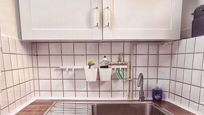 Ett kök med vita skåp, en bänkskiva i trä, en diskho i rostfritt stål och en kakelbeklädd vägg bakom diskbänken.