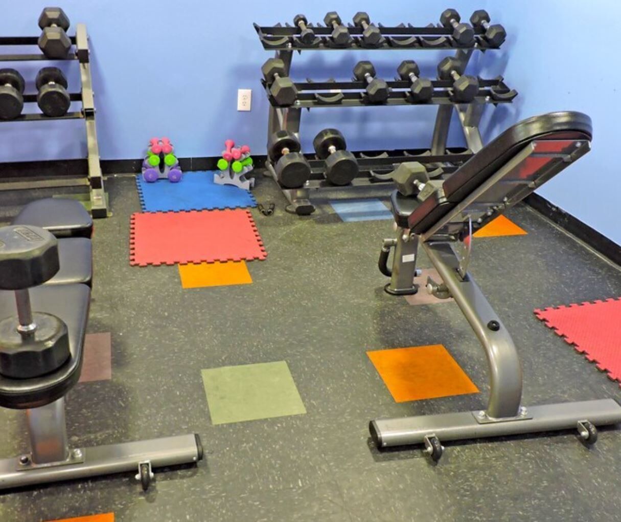 A gym with various exercise equipment, including dumbbells, a bench press, and a squat rack.