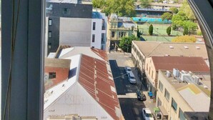 A view through a window of a cityscape with buildings, a road, and a sports field. - Light-filled Converted Warehouse 2 Bedroom Apartment in Prahran (Prahran)