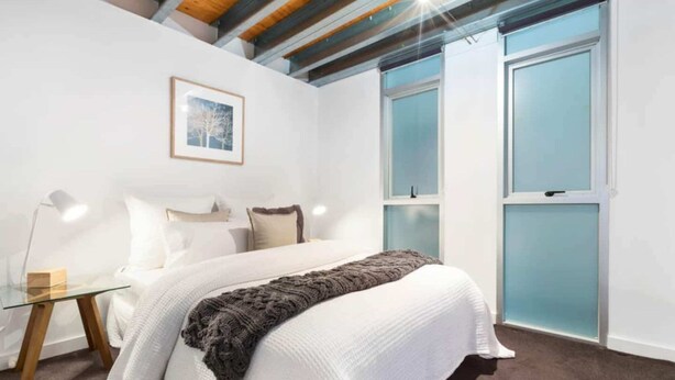 A bedroom with a bed, a glass table, and a framed picture on the wall. - Light-filled Converted Warehouse 2 Bedroom Apartment in Prahran (Prahran)