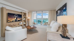 Una habitación de hotel moderna con un amplio ventanal que ofrece vistas a la ciudad, un televisor de pantalla plana montado en la pared y una zona de estar acogedora con un sofá y un sillón.