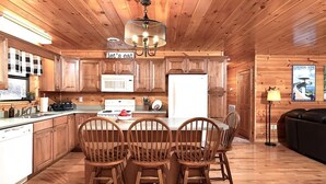 A wooden cabin-style kitchen with a dining table and chairs, a chandelier, and a refrigerator. - Private Mountain Cabin to Gather, Relax & Unwind near Pigeon Forge,TN (Sevierville)