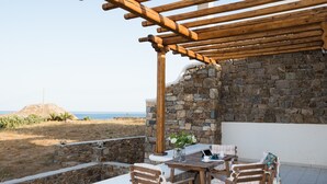 A stone wall with a wooden pergola and a table with chairs. - Case di Venia (Mykonos)