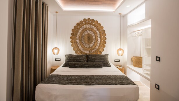 A modern bedroom with a large bed, a decorative wall piece, and a skylight. - Case di Venia (Mykonos)