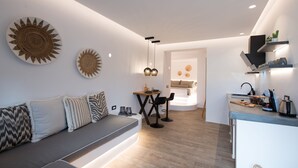 A modern kitchen with a built-in stove, a dining area with a table and chairs, and a living room with a sofa and decorative pillows. - Case di Venia (Mykonos)