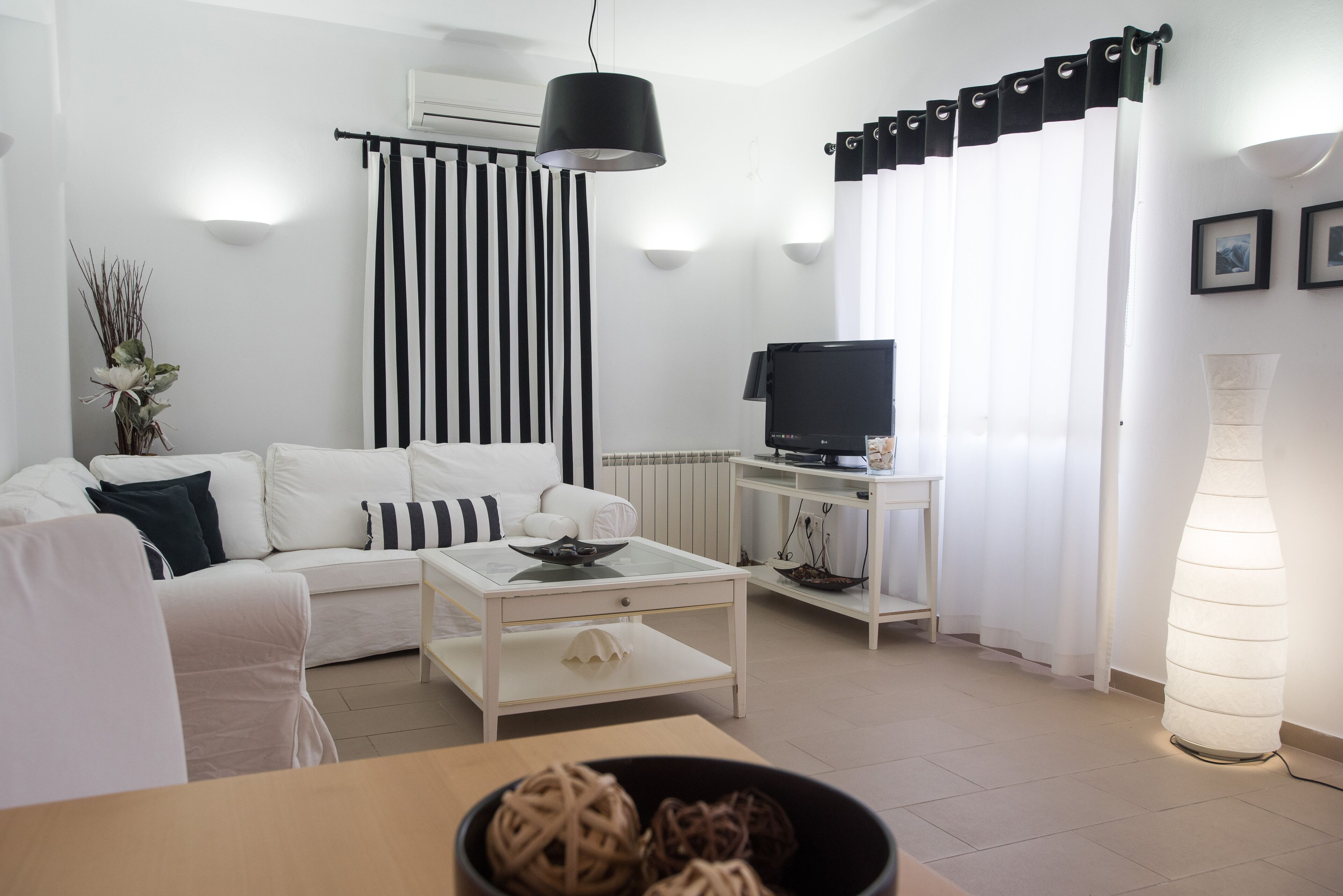 A modern living room with a white sofa, a coffee table, a TV, and a lamp.