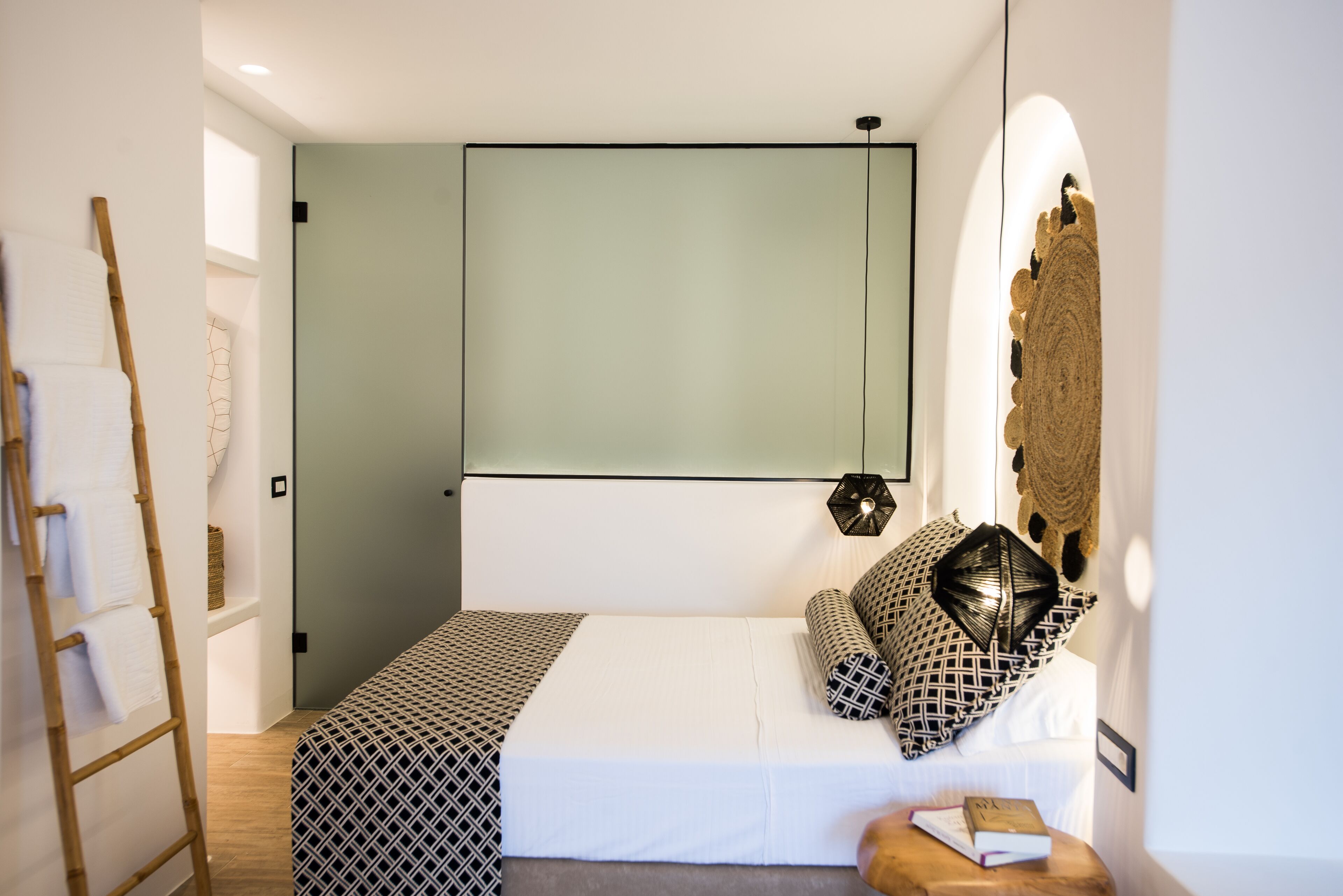 A modern bedroom with a bed, a wooden ladder, a wall-mounted light, and a decorative wall piece.