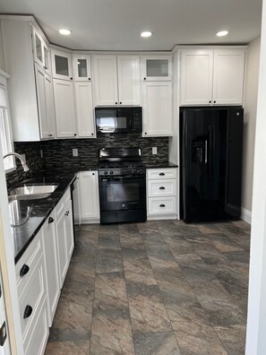 A modern kitchen with white cabinets, a black refrigerator, a microwave, and a stove.
