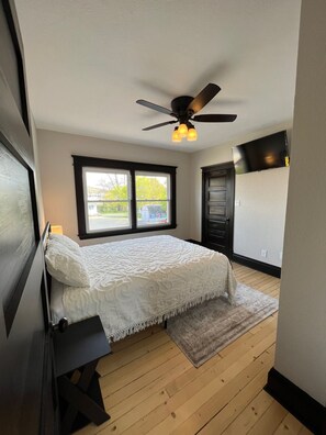 A bedroom with a bed, a ceiling fan, a window, and a TV.