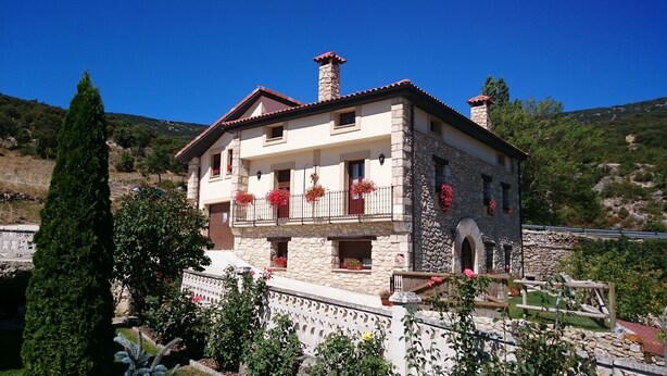 Un edificio de piedra de dos pisos con balcones, una entrada de piedra y un jardín circundante.