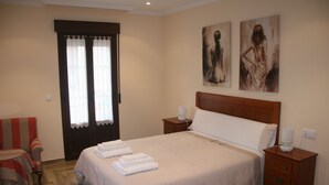 Un dormitorio ordenado con cama, dos mesitas de noche, una silla y cuadros en la pared.