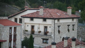 Un edificio de piedra de dos pisos con techo de tejas rojas, varios balcones con macetas de flores y una chimenea.