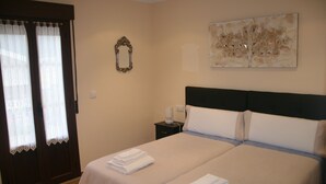 Una cama bien tendida con toallas dobladas, una mesita de noche con lámpara y un espejo montado en la pared.