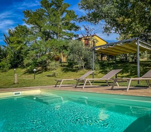Una piscina con agua cristalina, rodeada por una terraza de madera y sillas de descanso.