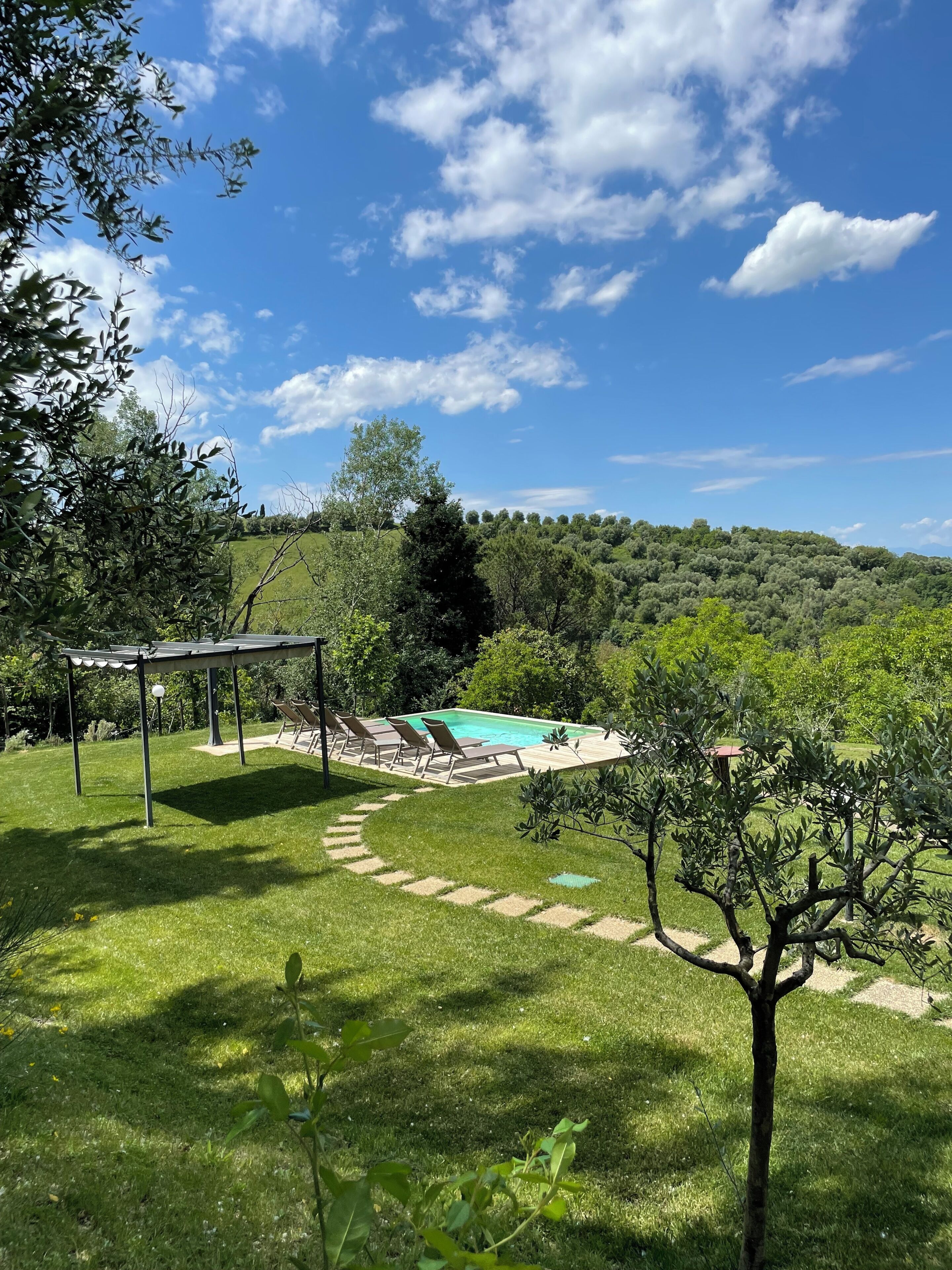 Patio con piscina, pérgola y vista a una colina arbolada.
