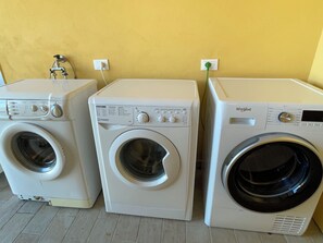 Three front-loading washing machines in a row against a yellow wall.