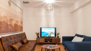 Uma sala de estar com um sofá de couro marrom, um sofá azul, uma mesa de centro de madeira e uma TV em um suporte de madeira.