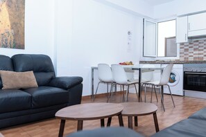 A compact living space with a sofa, dining table, chairs, and a kitchen area including a washing machine and oven. - Kasa Holiday apartment 2nd for 6. A step away from the Plya de Las Canteras (Las Palmas de Gran Canaria)