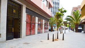 Um edifício com um portão preto identificado com o número '36', um caminho pavimentado e palmeiras.