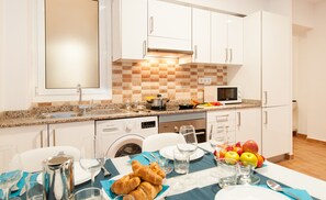 A modern kitchen with white cabinets, a granite countertop, and a dining area set for a meal. - Kasa Holiday apartment 2nd for 6. A step away from the Plya de Las Canteras (Las Palmas de Gran Canaria)