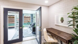A modern bathroom with a glass shower door, a wooden desk, a white chair, and a framed cactus picture on the wall. - Coffee Lovers Paradise (Scottsdale)