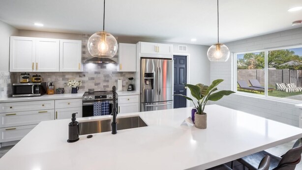 A modern kitchen with white cabinetry, stainless steel appliances, and pendant lighting. - Coffee Lovers Paradise (Scottsdale)