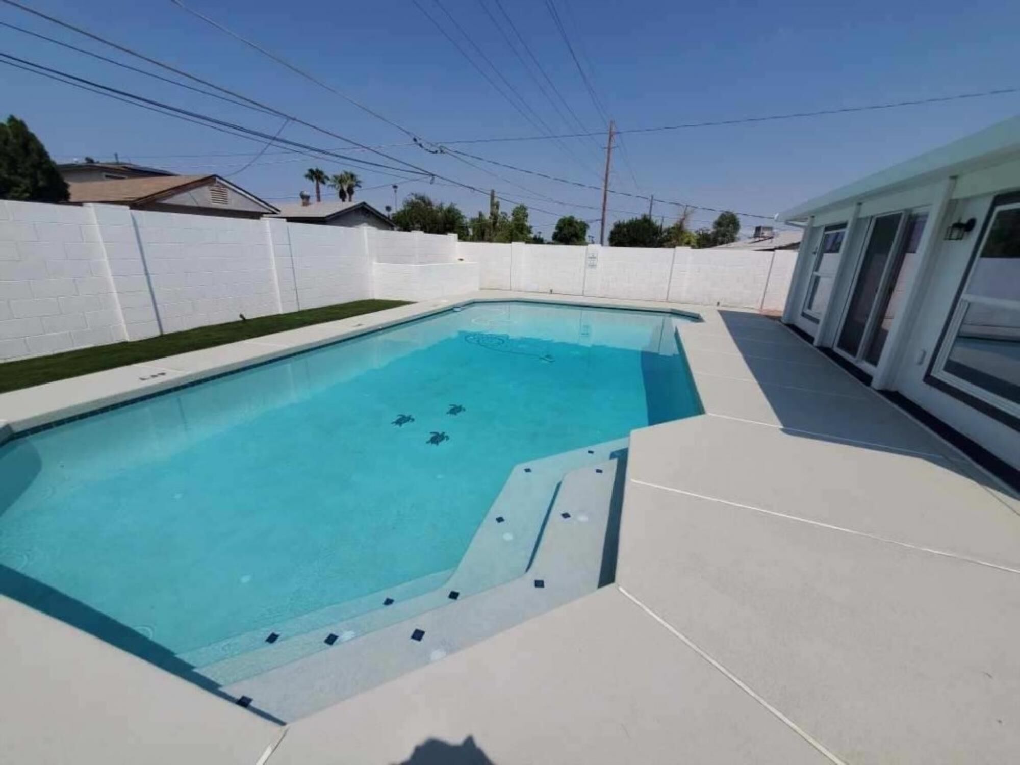 A rectangular swimming pool with a clear blue water surface, surrounded by a white fence and a tiled deck.
