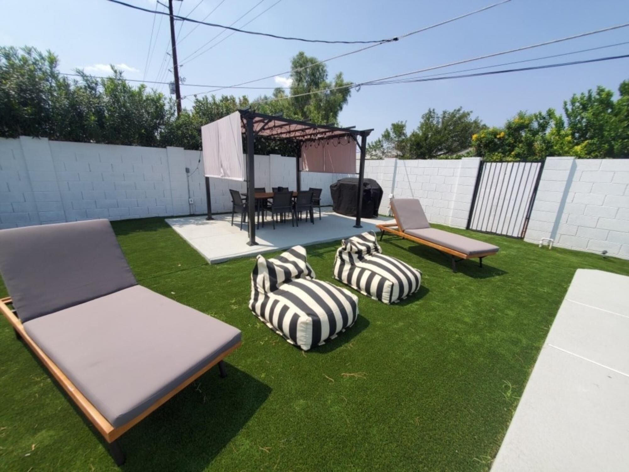 A backyard with artificial grass, a covered patio area, a barbecue grill, and outdoor furniture.