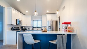 Una cocina moderna con armarios blancos, un refrigerador de acero inoxidable, un dispensador de agua y una máquina para hacer palomitas de maíz. Hay dos taburetes de bar y una pared de acento azul.