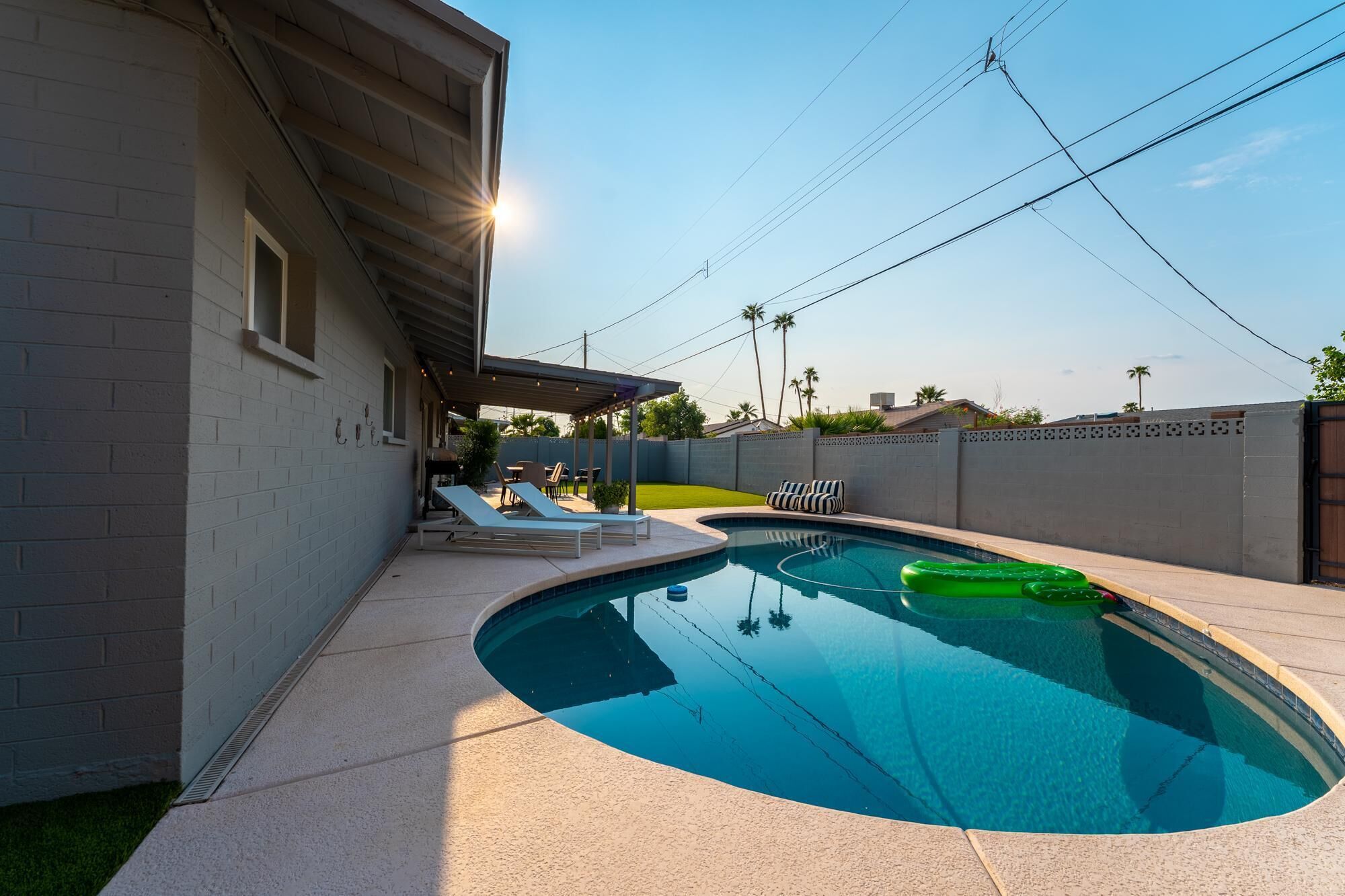 A swimming pool with lounge chairs, a covered patio, and a view of the neighborhood.