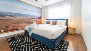 Un dormitorio con una cama grande, un ventilador de techo, una mesita de noche con lámpara y vistas a un paisaje desértico a través de una ventana.