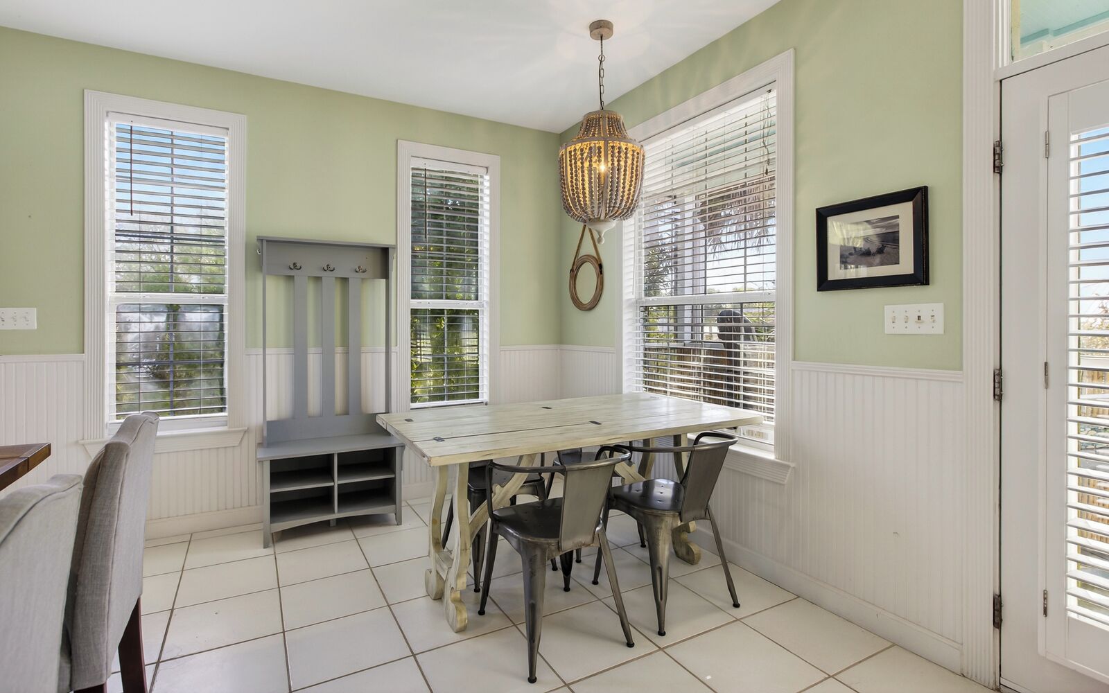 A dining area with a wooden table and chairs, a hanging light fixture, and windows with blinds.