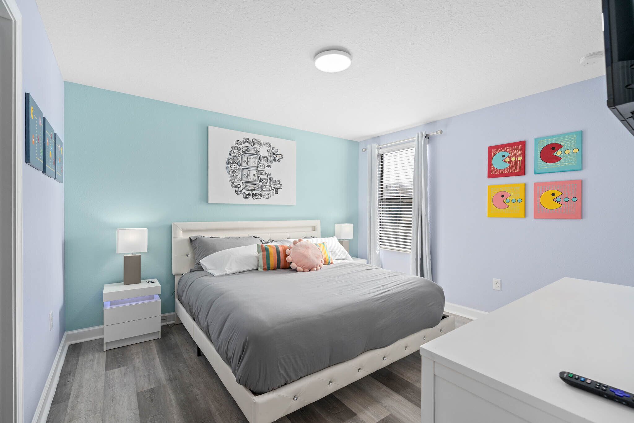 A bedroom with a bed, bedside tables, a desk, and wall art.