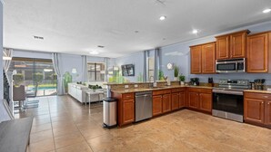 A modern kitchen with wooden cabinets, stainless steel appliances, and a large window overlooking a patio area. - 8BR Gaming Retreat, Pool & Theatre + 1 Night Free (Champions Gate)