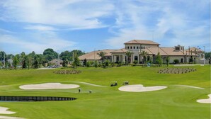 A golf course with sand bunkers and a large building in the background. - 8BR Gaming Retreat, Pool & Theatre + 1 Night Free (Champions Gate)