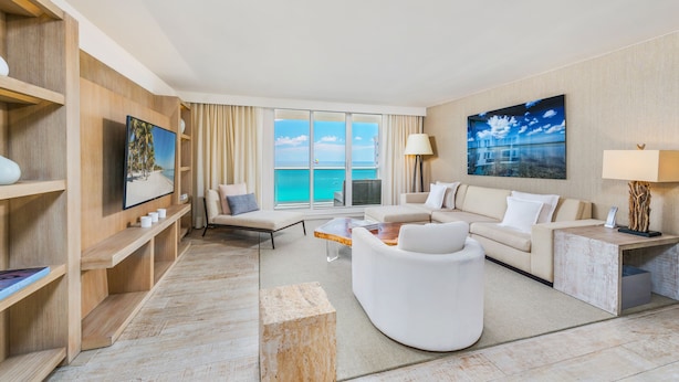 A modern hotel room with a large window, a sofa, a coffee table, and a TV.