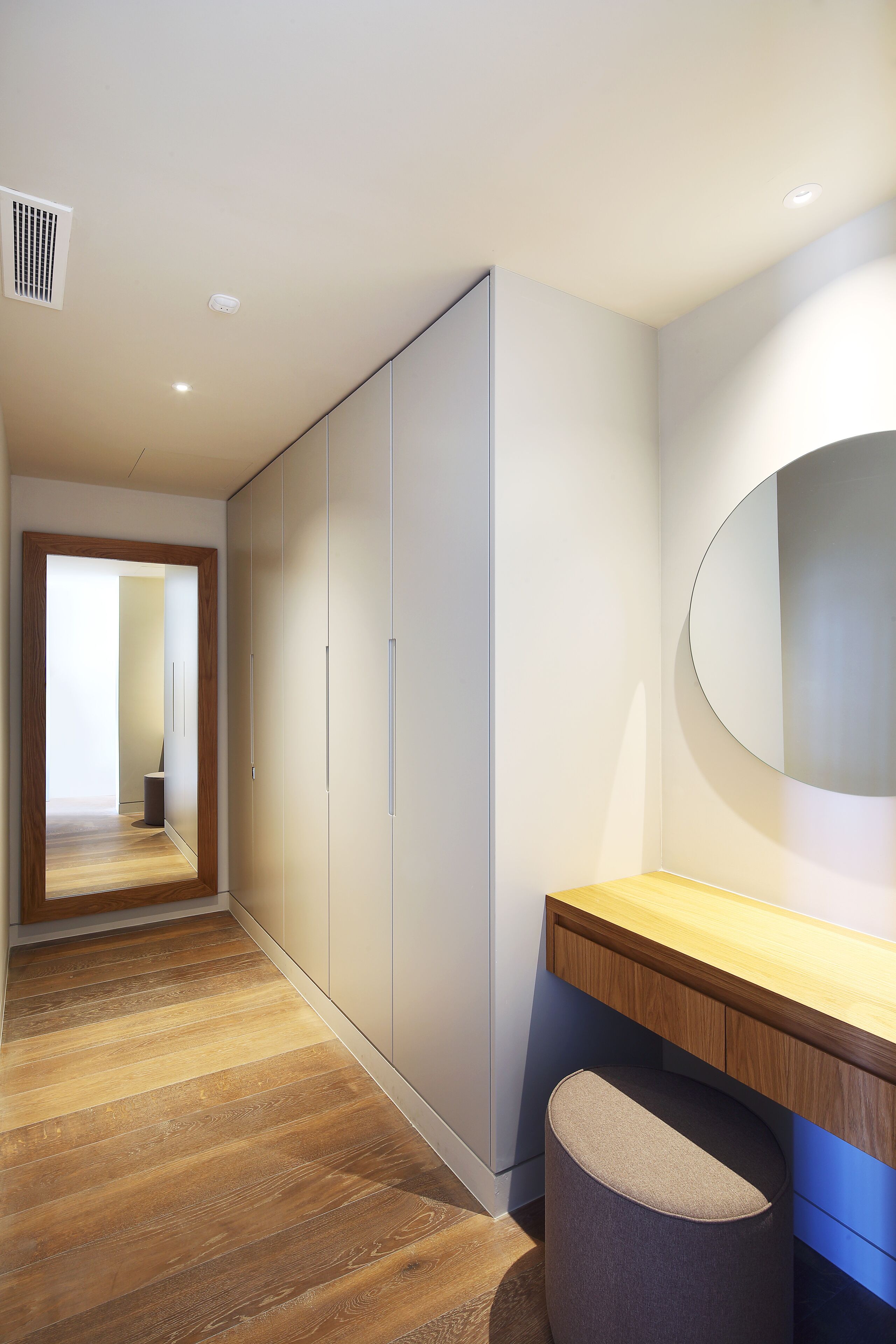 Un couloir doté d’un plancher en bois, d’un miroir, d’une armoire et d’un petit tabouret.