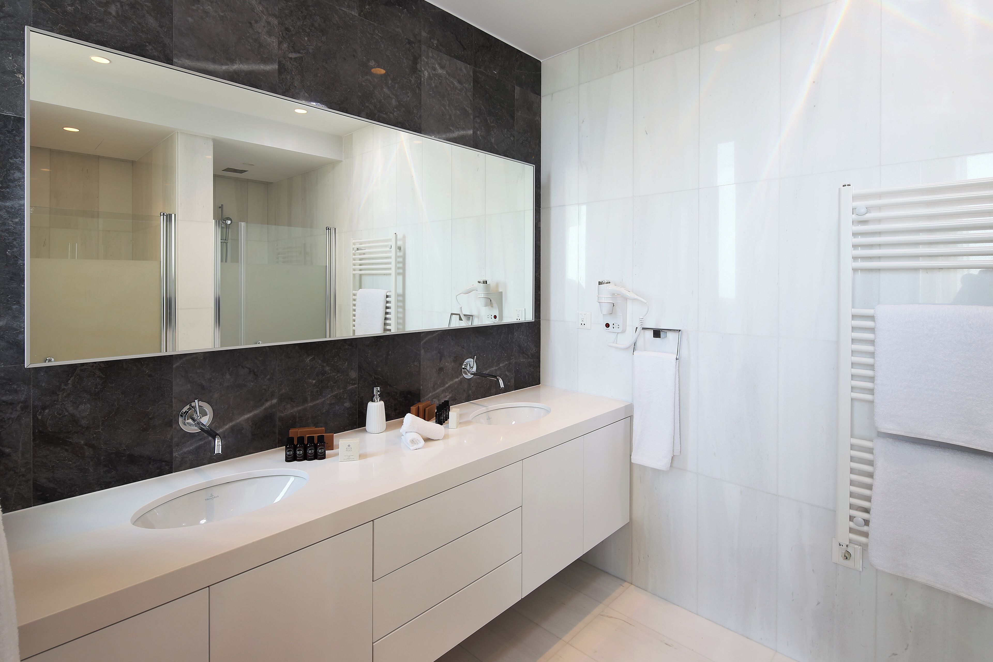 A modern bathroom with two sinks, a large mirror, and a towel rack.