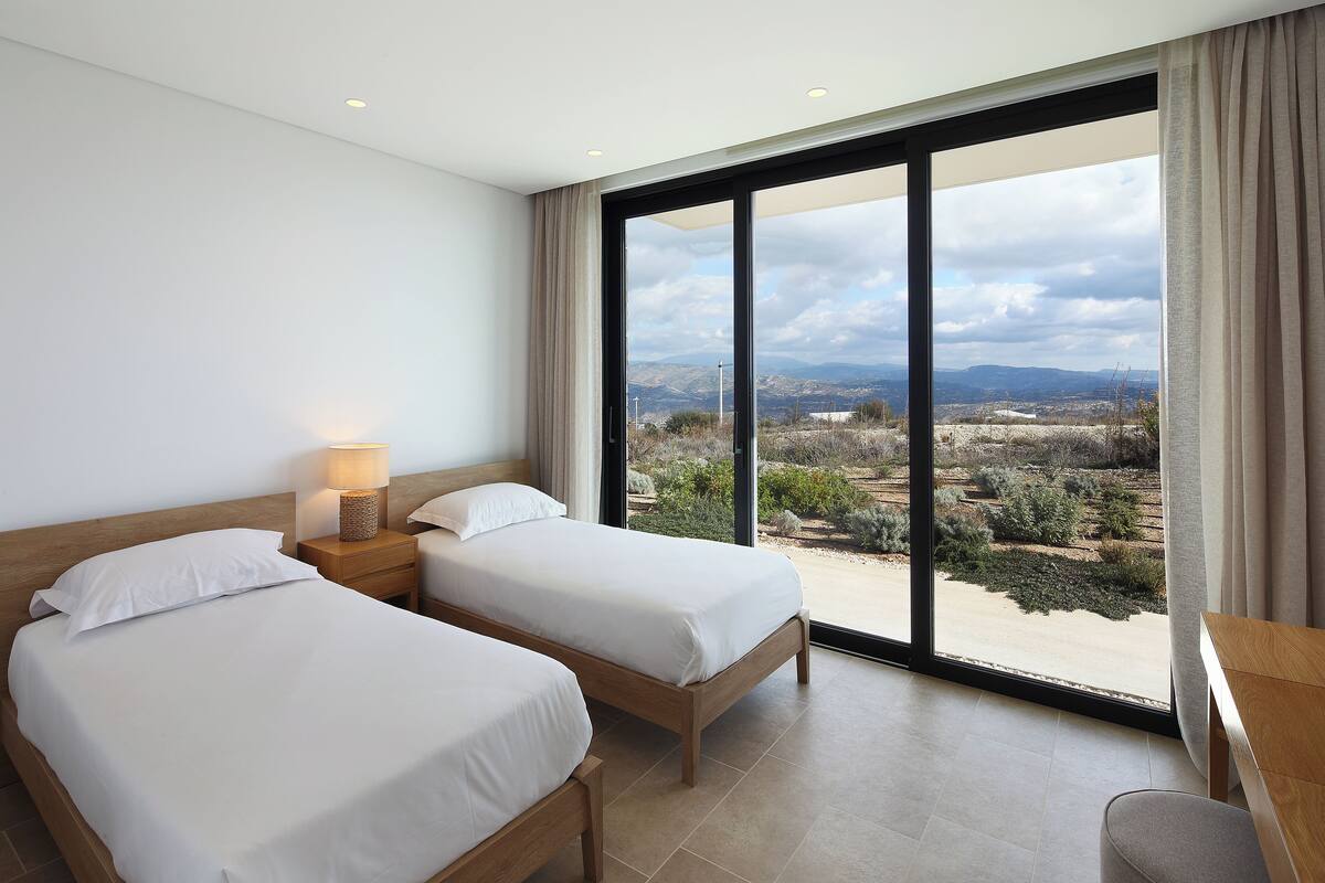 A hotel room with two beds, a desk, and a large window offering a view of the landscape.