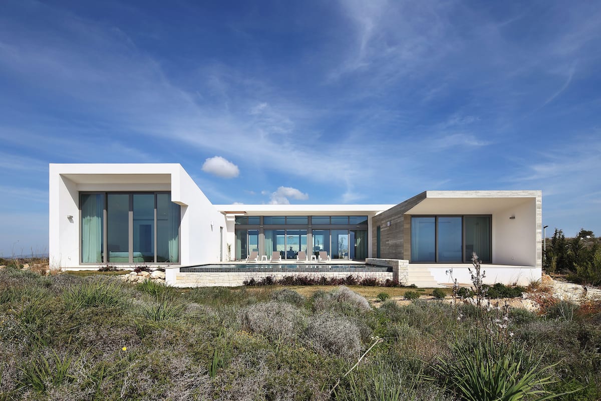 A modern two-story house with large glass windows, a swimming pool, and a landscaped garden.