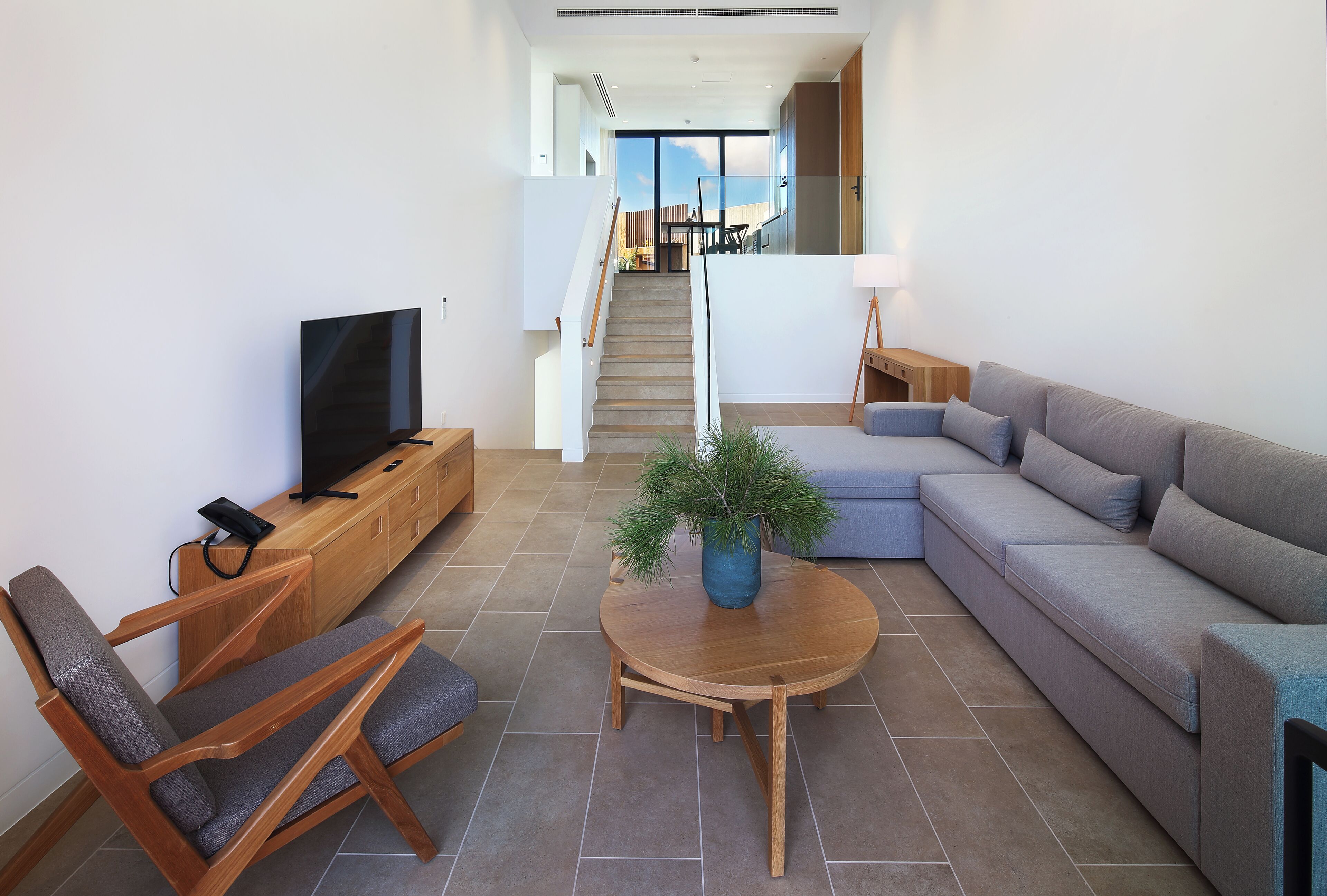 A modern living room with a sofa, a TV, a wooden coffee table, and a staircase leading to an upper floor.