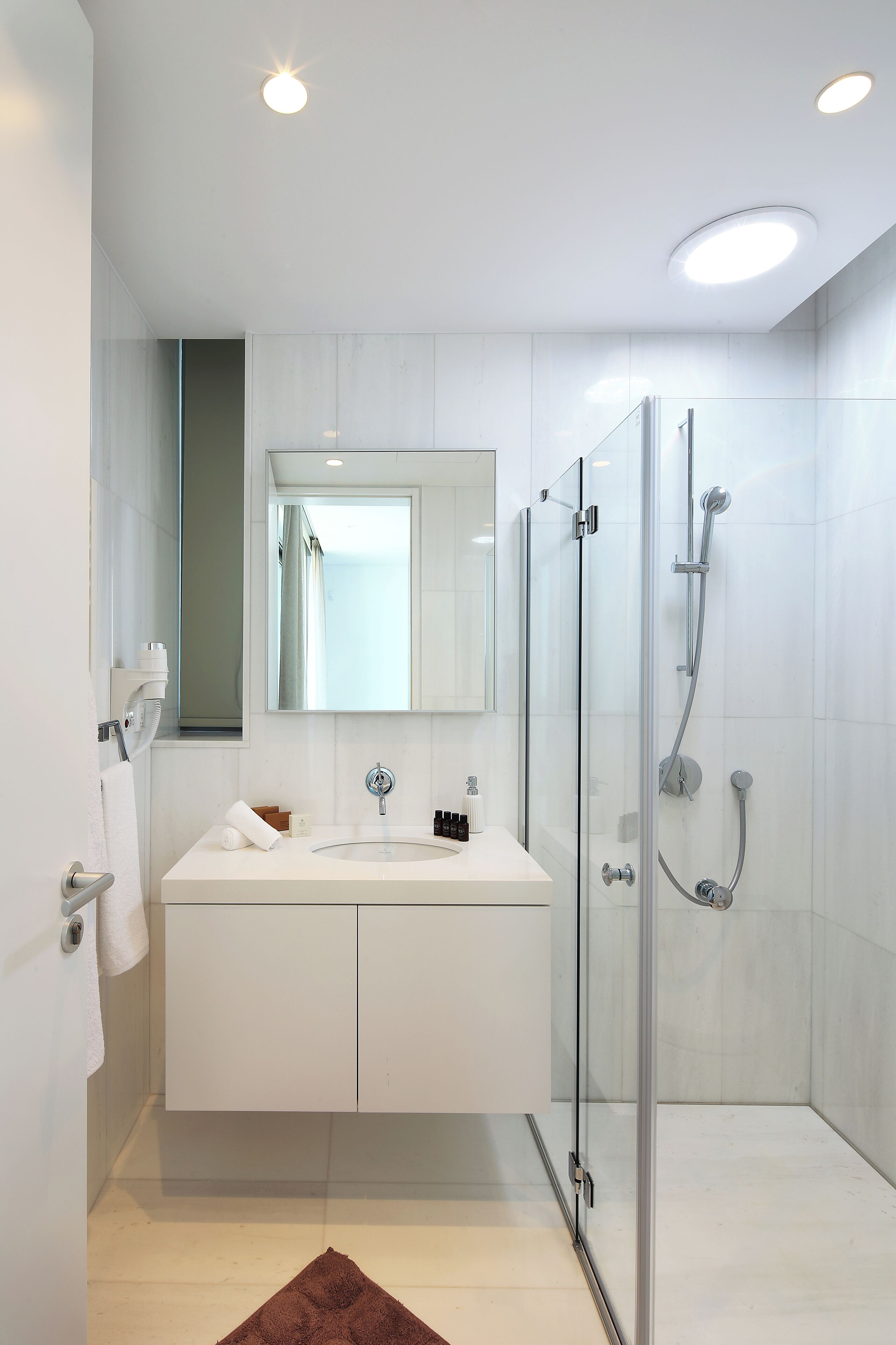 A modern bathroom with a glass-enclosed shower, a white vanity, and a large mirror.