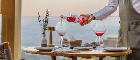 A table with two wine glasses, a vase with plants, and a bottle being poured into one glass.