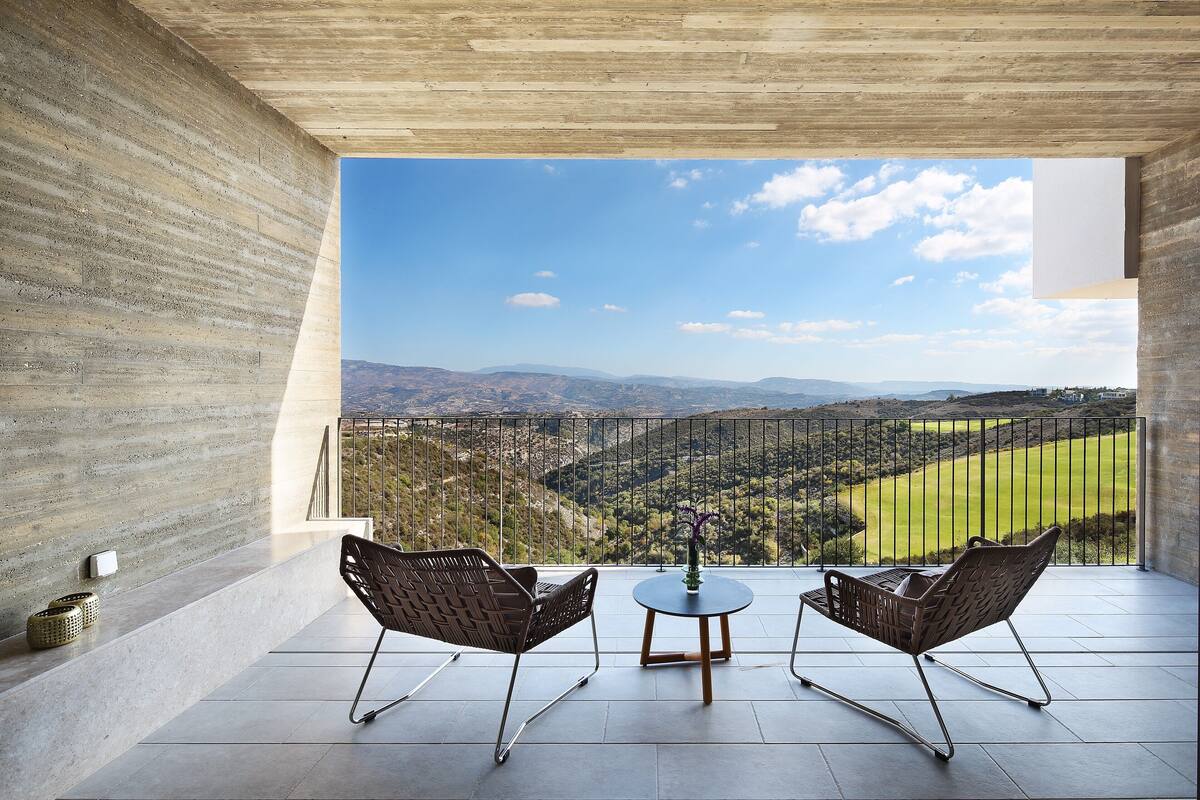 A balcony with two chairs and a table, overlooking a scenic landscape.