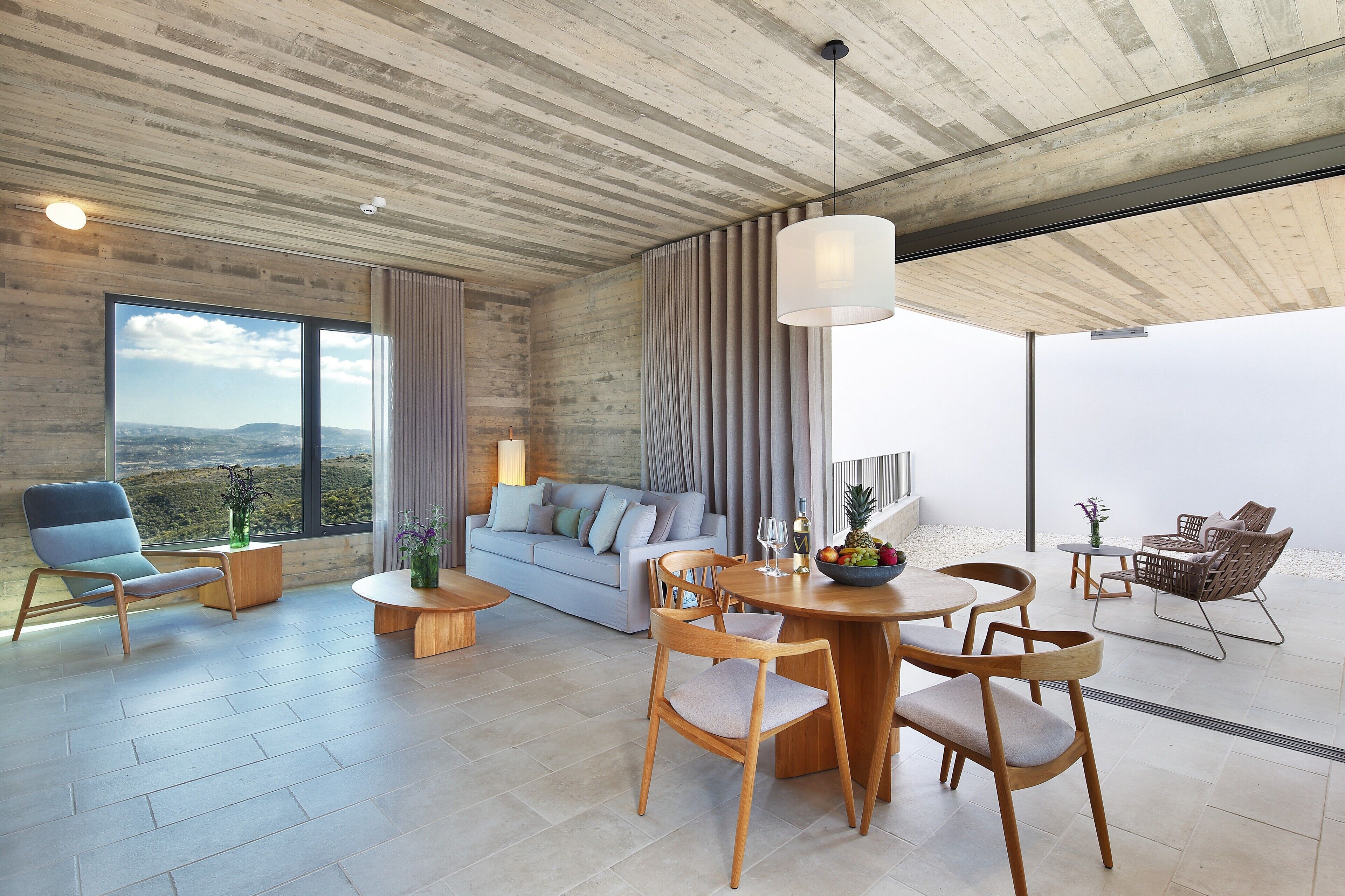Ein modernes Interieur mit Essbereich, einer Couch und Sesseln, großen Fenstern mit Blick und einer Holzzahl.