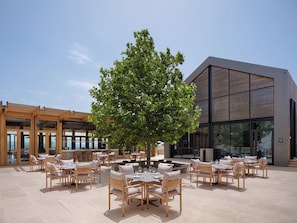 Enjoy dining under the shade of a large tree in a stylish outdoor setting with comfortable seating and large windows.