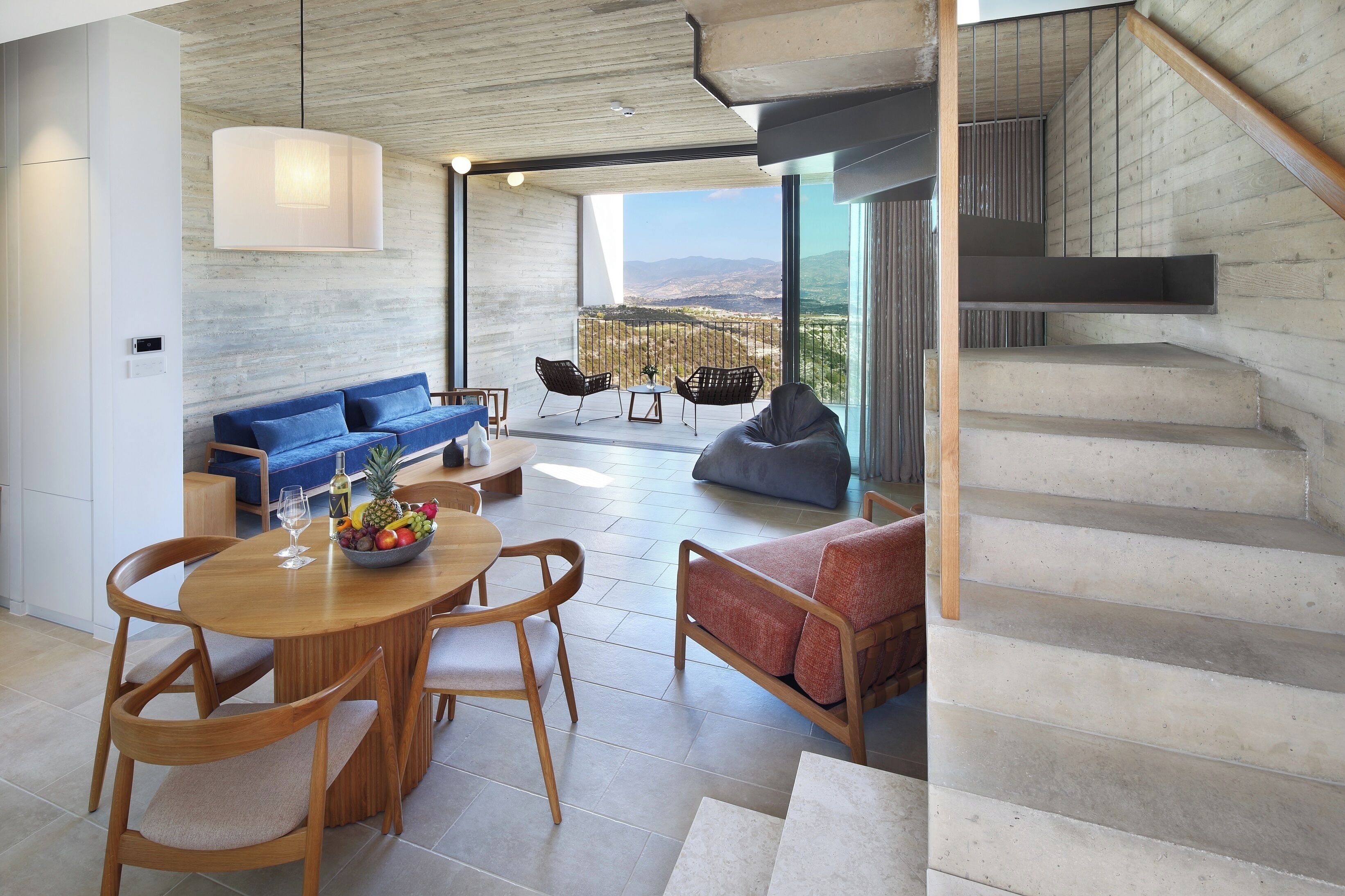 A modern living room with a dining area, a staircase, and a balcony with a view.