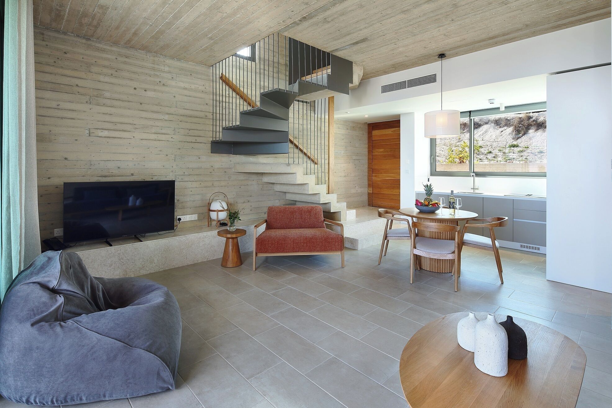 Una sala moderna con televisor, sofá, zona de comedor con mesa y sillas, y una escalera.