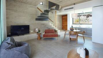 Una sala moderna con televisor, sofá, zona de comedor con mesa y sillas, y una escalera.